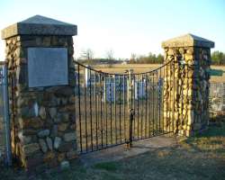 The graveyard is boarded with wire fencing and there is an arched stone entrance through an iron gate.